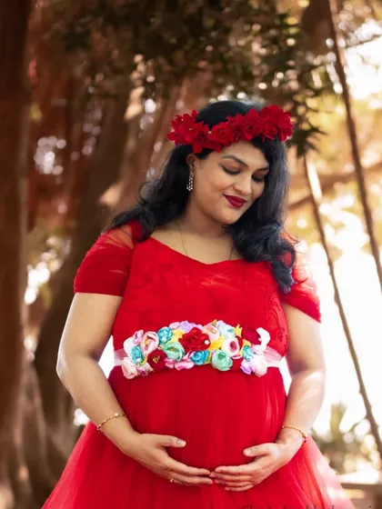 A close-up of a client looking serene in our red maternity gown, accessorized with a floral crown and belt for a soft, natural look.