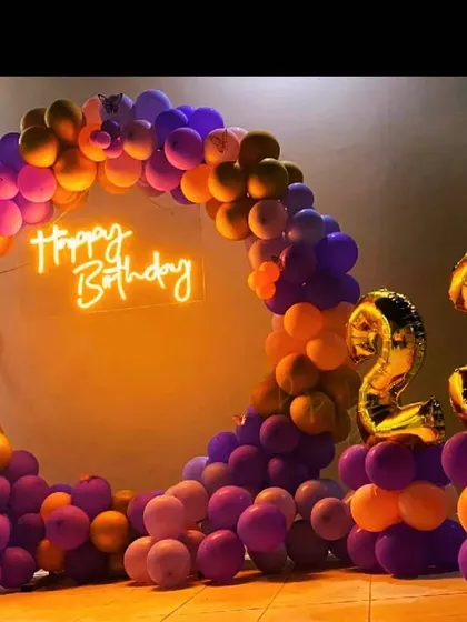 A bold and colorful 23rd birthday decoration. The circular balloon arch in shades of purple and orange is paired with gold foil number balloons for a fun and energetic vibe.