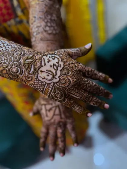 A close-up of the bride's palm, featuring the name "Akbar" written in beautiful calligraphy, surrounded by intricate floral patterns.