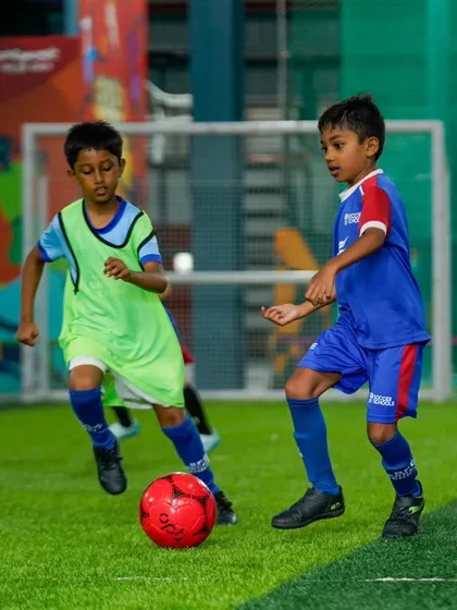 Two players challenge for a bright red ball during a small-sided game. These matches maximize touches and improve decision-making in tight spaces.