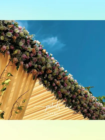 A close-up of the floral canopy on the contemporary mandap. The mix of assorted roses against the bright yellow fabric and blue sky creates a breathtakingly colorful and romantic image.