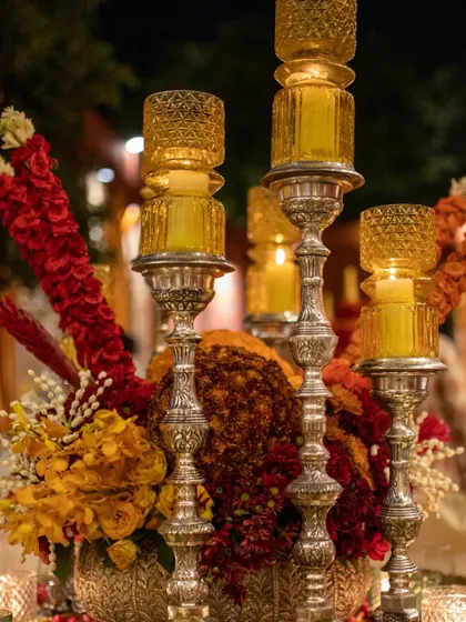 The warm glow of the candles illuminates the silver candelabras and the rich textures of the floral arrangement. The design is perfect for a grand, traditional celebration.
