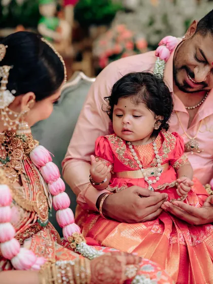 A family captured during a ceremony. The baby girl's red pattu pavadai, with its delicate gold embroidery, was custom-made to be the star of the show.
