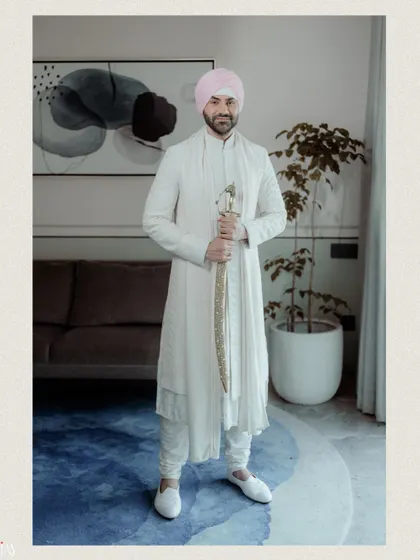 A full-length portrait of the Sikh groom in his elegant all-white attire and pink turban.