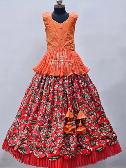 A Kalamkari print lehenga with an orange peplum top. The traditional print on the skirt is given a modern twist with the stylish top and net ruffle at the hem.