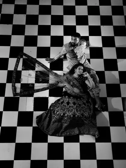 A creative black and white shot of a couple in traditional attire on a checkerboard floor. The high-angle perspective and graphic pattern make for a unique and artistic portrait.