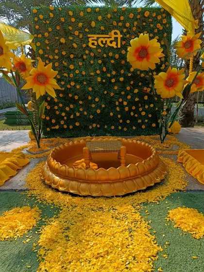 A stunning sunflower-themed Haldi setup. The backdrop of greenery adorned with large, bright sunflowers and a traditional urli for the ceremony creates a cheerful and sunny atmosphere.