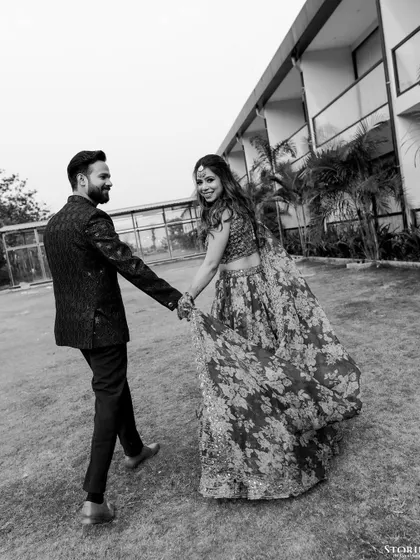 A playful "follow me to" style shot in black and white, capturing the bride's joyful expression as she leads her partner.