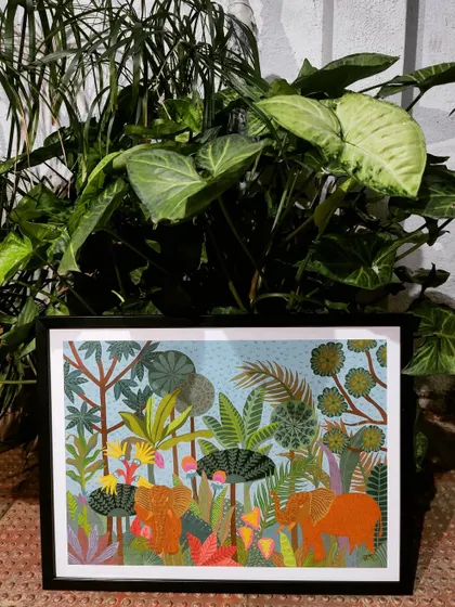 Here is the finished, framed tropical elephant painting, ready to be displayed. The artwork is placed in front of a real plant, showing how it can enhance and complement a home's green spaces.