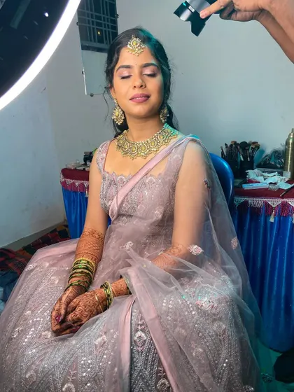 A full view of the bride seated for her Sangeet look, with the ring light showing off the flawless makeup application.