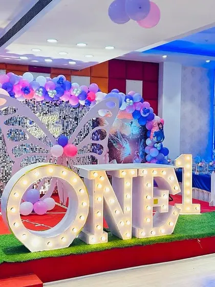 A magical fairytale-themed first birthday party. The setup combines elements of fairies and butterflies with a castle backdrop, marquee letters, and a green turf floor.