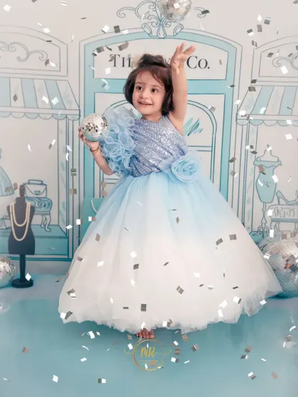 A playful and stylish toddler photoshoot with a "Tiffany & Co." theme. The little girl is dressed in a beautiful blue gown, tossing confetti and celebrating in a custom-designed set.