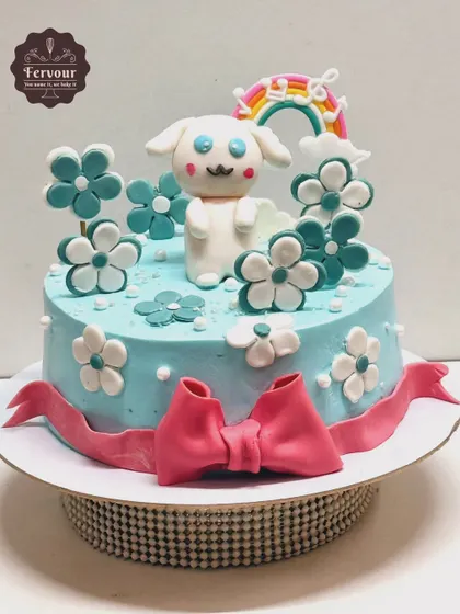 A sweet Cinnamoroll-themed cake in pastel blue. The design features the adorable character surrounded by flowers and a rainbow, making it a cute choice for a birthday.