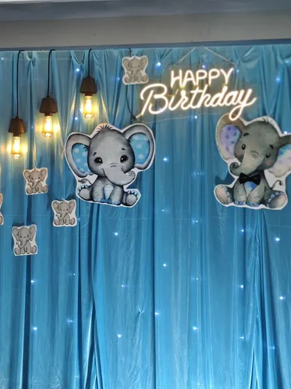 A simple and sweet baby elephant backdrop with a neon 'Happy Birthday' sign and hanging industrial-style lights for a modern twist.