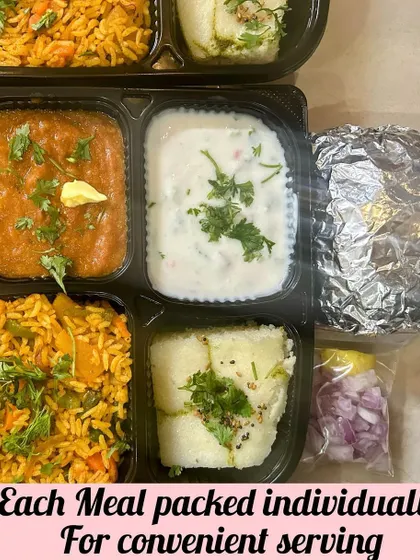 Each meal is packed individually for convenient serving. This box includes Pav Bhaji with a pat of butter, Tawa Pulao, Raita, and Sandwich Dhokla.