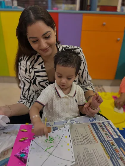 A mother and son work on a finger-painting craft to decorate a paper kite, a great sensory and creative experience.