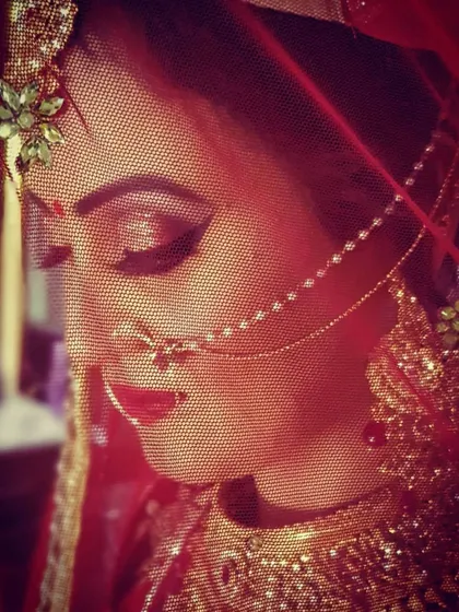 Another artistic shot through the bride's veil. The red lighting enhances the warmth of her makeup, highlighting the red lip and the dramatic eye contour.