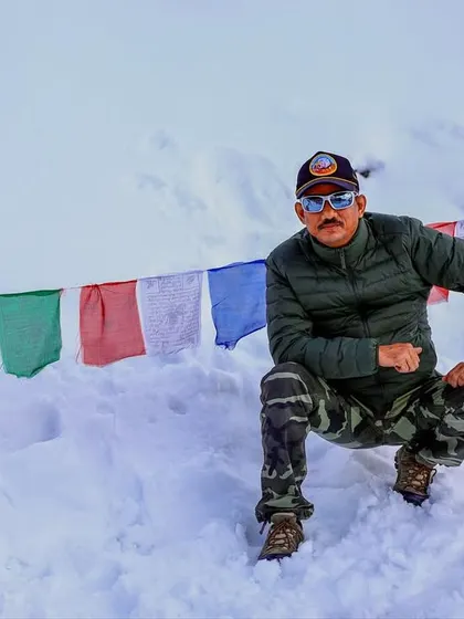 A member of our team posing in the snow at Khardungla Pass. The vibrant prayer flags add a splash of color to the white landscape.