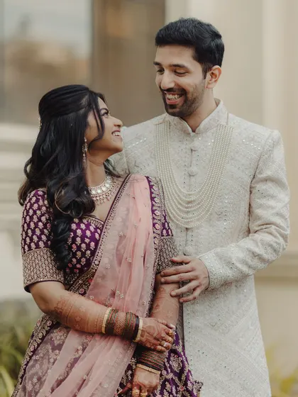A happy couple at their reception. Her makeup is a soft glam look with a hint of purple to match her beautiful lehenga, creating a cohesive and elegant style.