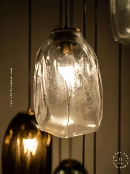 This cascading installation features pendants made of organic, free-form glass in smoked and amber tones. The textured, irregular shapes create a beautiful, water-like effect, perfect for adding a sense of calm and artistry to a room.