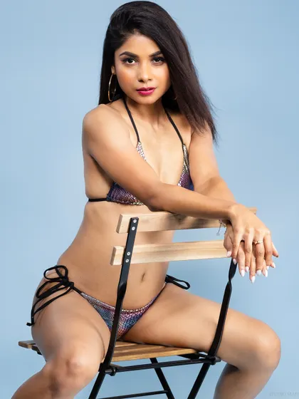 A model seated on a chair in a shimmering snakeskin-print bikini against a cool blue background. This demonstrates my use of color to complement swimwear fashion.