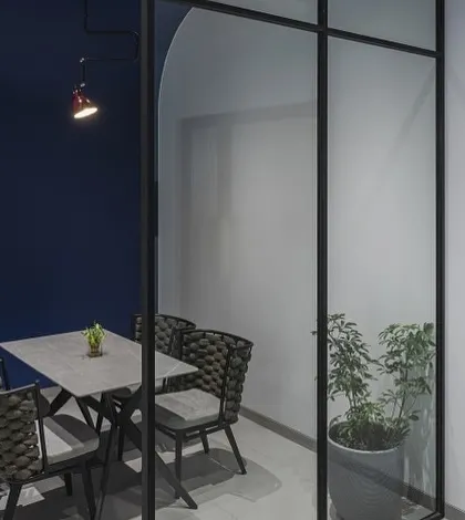 This modern meeting room in a Mumbai office is defined by its glass partitions and a bold blue accent wall. The design fosters a sense of calm and focus, creating a sophisticated space for collaboration and client meetings.
