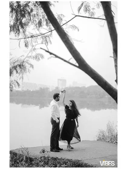 A black and white photo of a couple dancing by a lake. The serene background and their gentle movement create a timeless and romantic image.