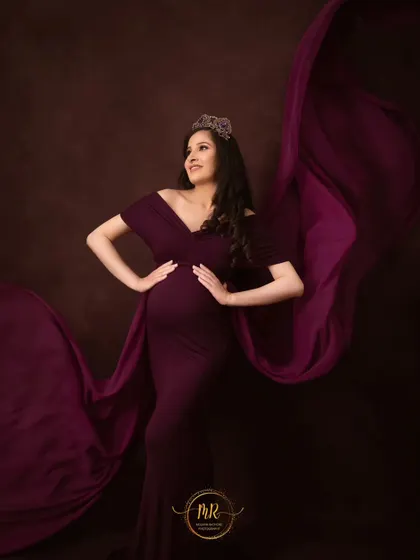 A confident and regal pose in a deep purple gown and crown. The flowing fabric adds a sense of drama and movement to this beautiful solo maternity shot.
