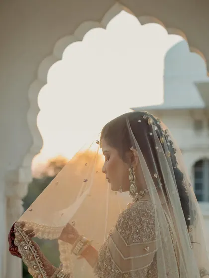 A beautiful, sun-drenched bridal portrait, with the bride gently holding her veil against the backdrop of a palace archway.