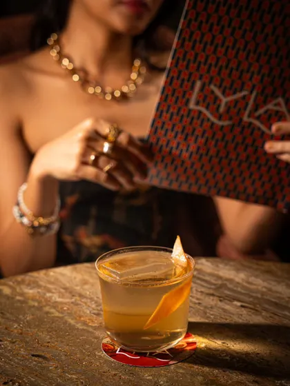 A person holding a menu while a perfectly styled cocktail sits in the foreground at Lyla Bombay. This shot connects the drink to the experience of exploring the menu.