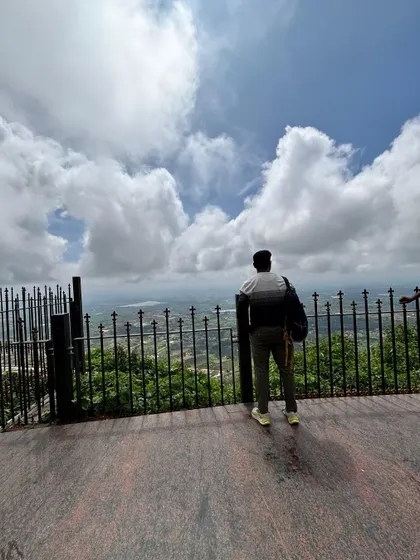 A traveler looking out from a viewpoint, with a vast landscape and cloudy sky ahead. A moment of awe and wonder.