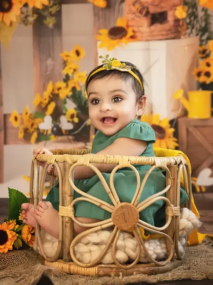 A baby girl smiles brightly in a wicker basket, surrounded by a cheerful sunflower setup.