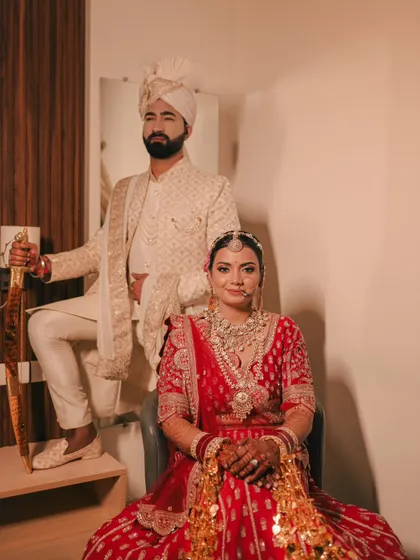 A royal and powerful portrait. The bride is seated while the groom stands beside her with a ceremonial sword, creating a regal and traditional image.