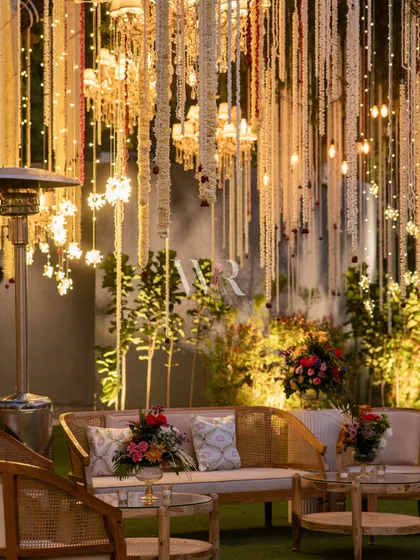 An intimate lounge setting with natural wood furniture, set against a backdrop of cascading mogra and chandeliers. This space provided a serene corner for guests to relax during the wedding festivities.