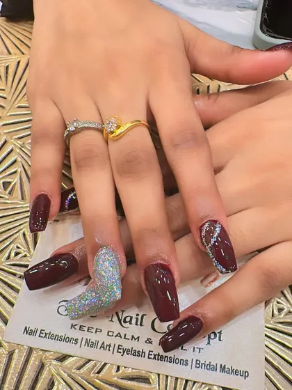 A bold and dramatic set of long, square-shaped nails. The deep maroon polish is paired with two different accent nails: one with full holographic glitter and another with a silver glitter wave design.