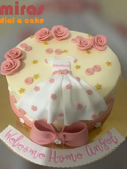 "Welcome Home Angel." This lovely cake celebrates a baby's arrival with a delicate fondant dress, pink roses, and tiny stars, creating a warm and loving welcome.
