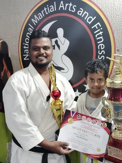 This yellow belt student celebrates his third-place win with two trophies, showing that success starts early at NMFA.