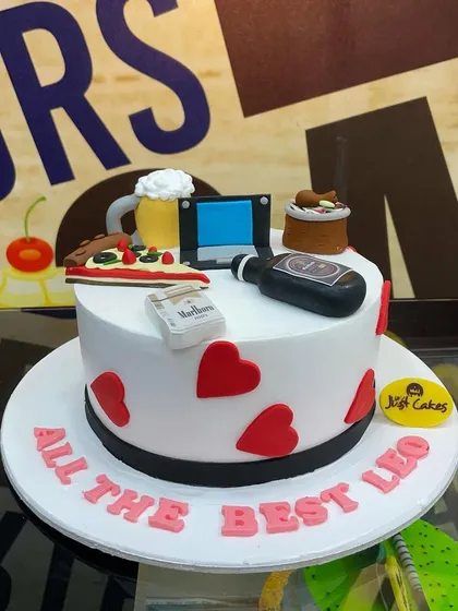 A 2kg "essentials" cake for a fun celebration, topped with fondant pizza, beer, a laptop, and other personal items.