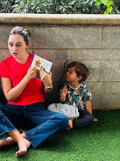 A mother reads a story to her two sons on the grass during our Tomatina celebration, a quiet moment amidst the fun.