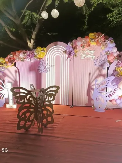 Another view of the butterfly-themed birthday party, showing the setup under the hanging lanterns at night. The lighting adds a magical touch to the decor.