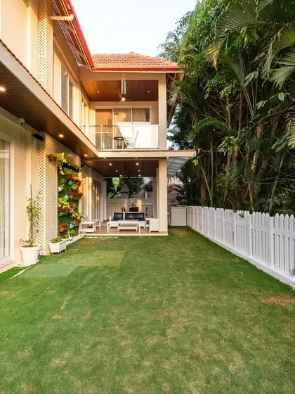 The villa's backyard features a pristine lawn, a classic white picket fence, and a covered patio area, creating a private and serene outdoor environment.