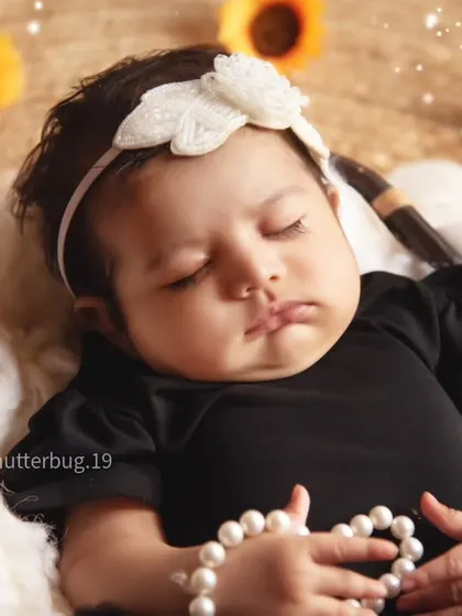 A sleeping newborn girl looking angelic in our sunflower-themed setup, holding a string of pearls.