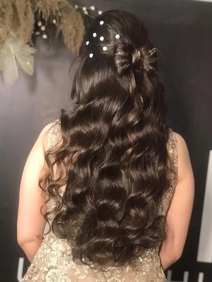 For this party look, we created a half-up hairstyle with a bow made of hair. The rest of the hair was styled in long, flowing curls and decorated with delicate pearl pins for a touch of elegance and romance.