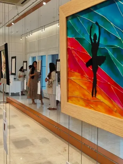 A view of the 'Finding Solace' exhibition, with a colorful glass painting of a ballerina's silhouette in the foreground.