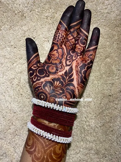 A lovely stained hand adorned with bangles, showing how beautiful a mature henna design looks with traditional accessories.