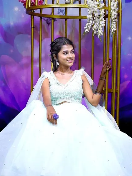 A young model in a beautiful light blue gown, posing in a birdcage prop against a magical floral backdrop.