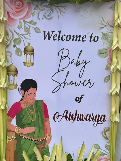 A personalized welcome sign for Aishwarya's baby shower, framed with traditional decorations made from coconut leaves.