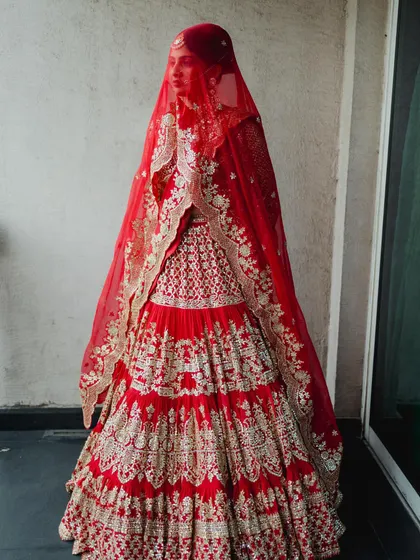 A full-length view of this magnificent tiered bridal lehenga in a classic red. The detailed gota patti work and the dramatic double dupatta created a truly regal silhouette for the bride's grand entrance.