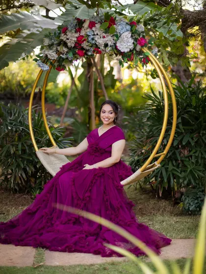 A full-length portrait on the floral swing, showcasing the beautiful drape of the purple gown.