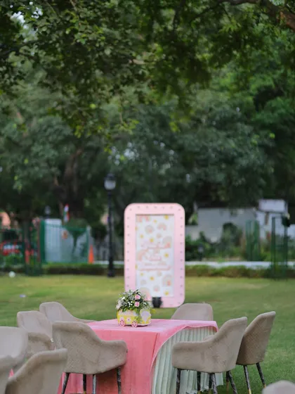 A distant view of the outdoor party setup, showing the guest tables and a pink marquee sign in the background, creating a beautiful scene amidst the lush greenery.